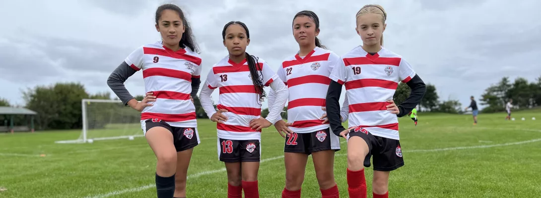 Four girls standing together on the field posing for a picture with soccer balls