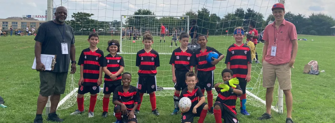 Youth boys soccer team posing in front of goal with coaches