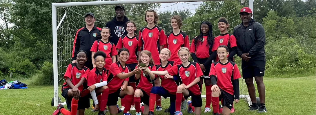 Girls youth soccer team posing in front of goal with coaches