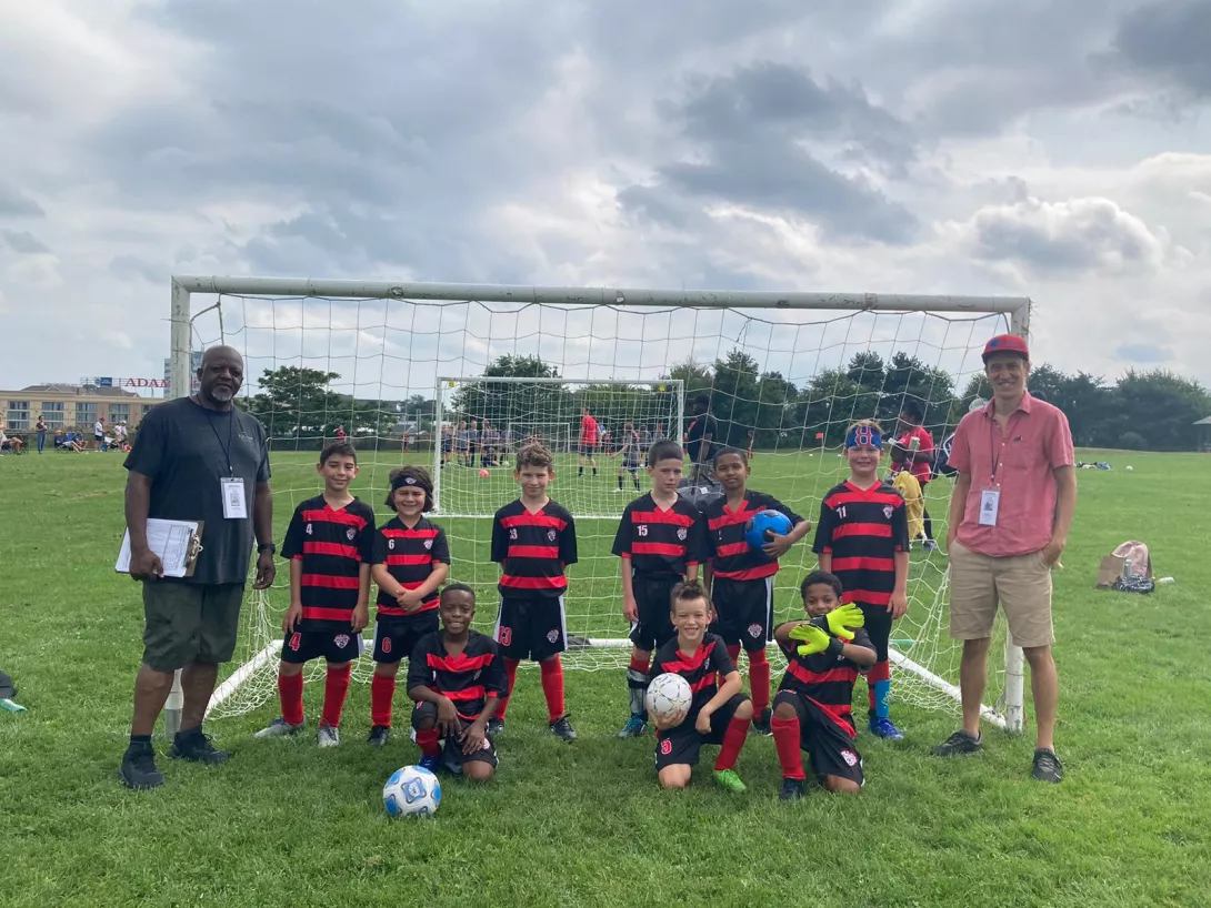 Youth boys soccer team posing in front of goal with coaches