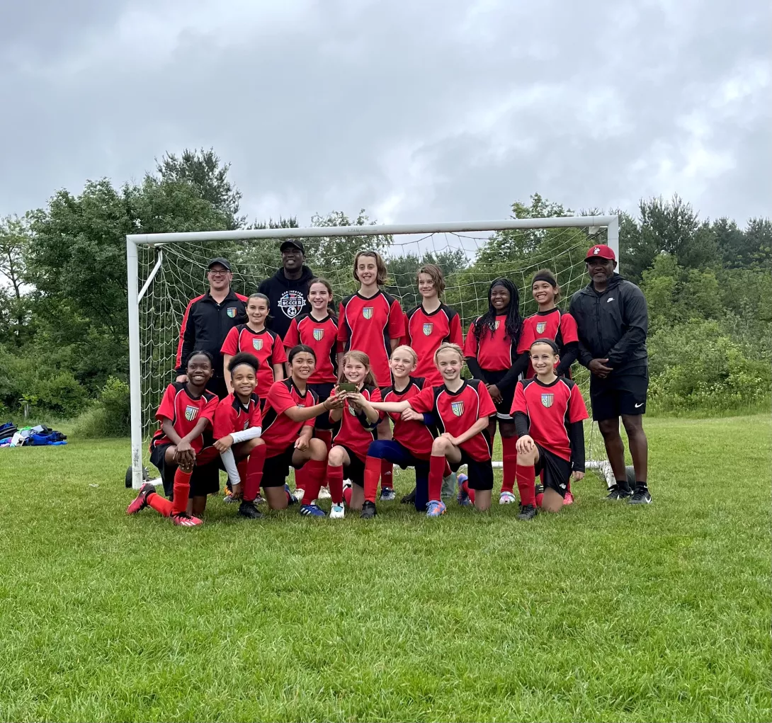 Girls youth soccer team posing in front of goal with coaches